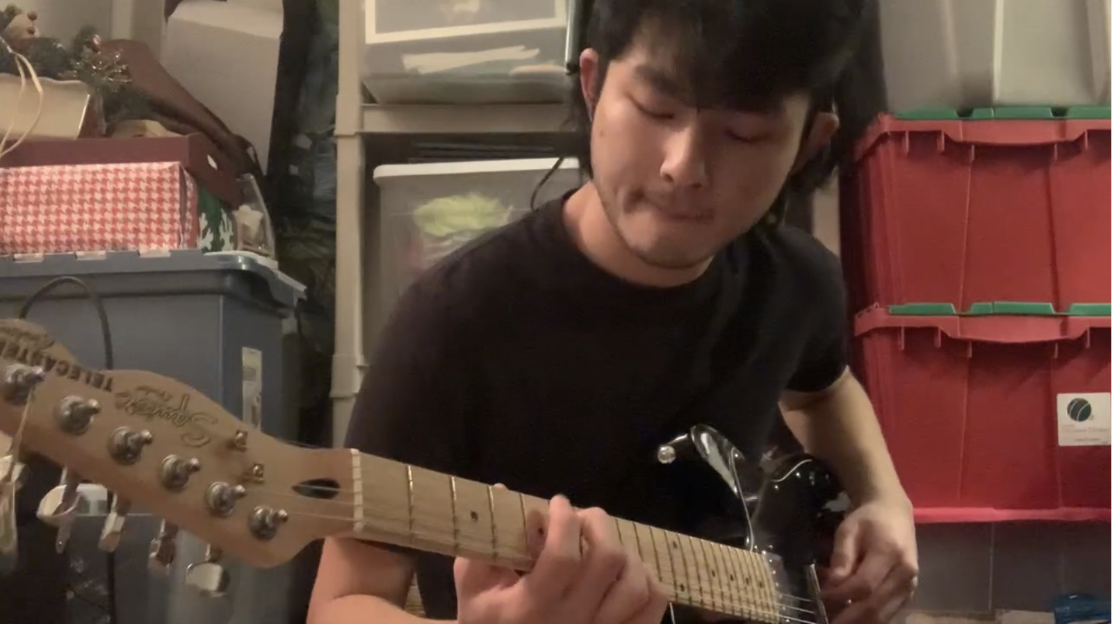 Student playing guitar with boxes of Christmas decoration in the background